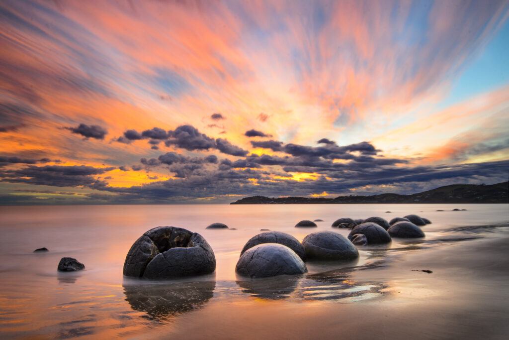 The famous Moeraki boulders lie scattered along a beach about an hour’s drive north of Dunedin. According to Māori legend, the boulders are gourds washed from the great voyaging canoe Araiteuru when it was wrecked upon landfall some 1,000 years ago.
Scientists explain the boulders as septarian concretions formed about 65 million years ago. Crystallisation of calcium and carbonates around charged particles in muddy undersea sediments gradually formed the boulders in a process taking as long as 4 million years.